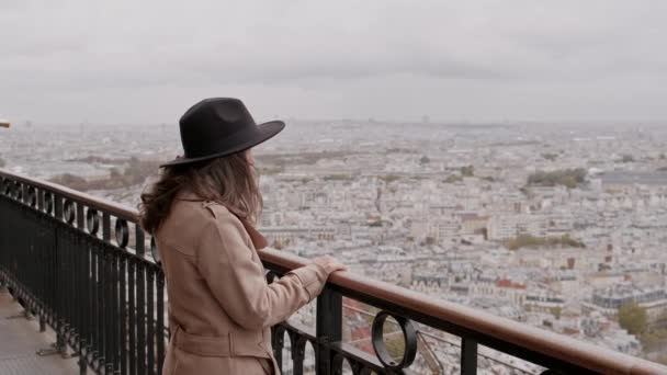 Vídeo de una joven con sombrero y abrigo negro mirando la ciudad de París desde la Torre Eiffel. - Imágenes, Vídeo