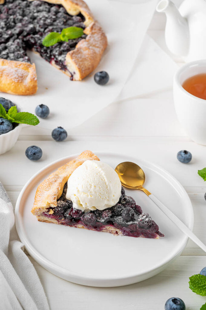 ブルーベリーガレット,オープンパイ,または白い木のテーブルにアイスクリームと紅茶のカップとタルト. サマースイートパイ - 写真・画像