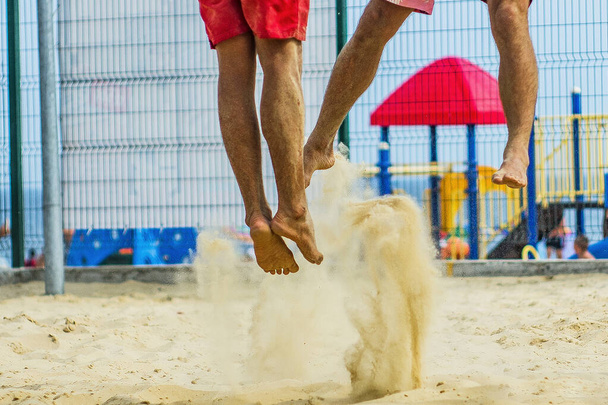 Nohy volejbalistů ve skoku s cákancemi písku zblízka - Fotografie, Obrázek
