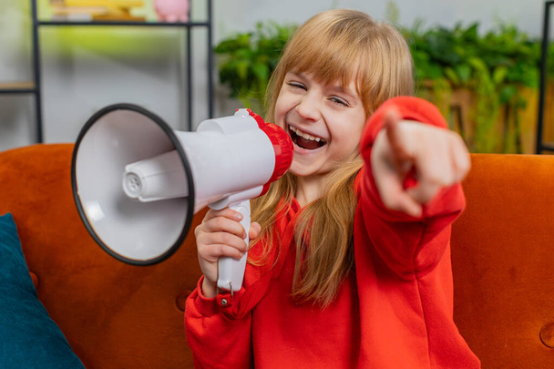 Muotokuva teini lapsi tyttö puhuu megafoni, julistaa uutisia, äänekkäästi ilmoittaa mainos varoitus käyttäen kaiutin huutaa puhetta. Teini pieni lapsi kotona olohuoneessa sohvalla - Valokuva, kuva