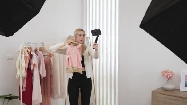 Młoda medialna kobieta twórca treści społecznych zrobić film mody przy użyciu selfie stick. Blogger uśmiech do kamery podczas dokonywania przekonujące ubrania online sprzedają vlog do publiczności lub zwolennika. Blithe - Materiał filmowy, wideo