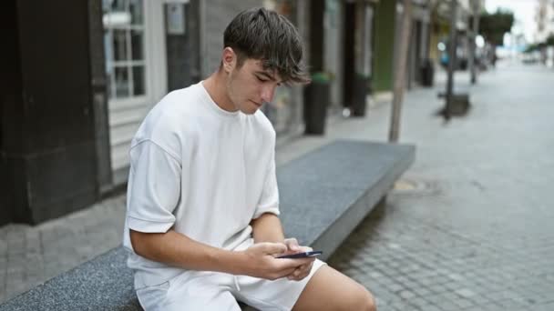 Podekscytowany młody latynoski nastolatek, zwycięzca, świętujący na ulicy miasta podczas korzystania z telefonu komórkowego, pisząc radosną wiadomość na świeżym powietrzu. - Materiał filmowy, wideo