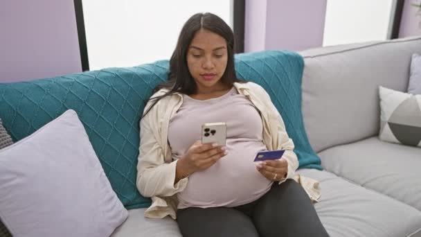 Glowing expectant young woman, chilling on sofa at home, enjoying online shopping with phone & credit card - Footage, Video