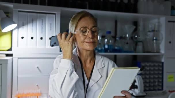 Mujer madura científica examinando notas en un entorno de laboratorio, evocando concentración y experiencia - Imágenes, Vídeo