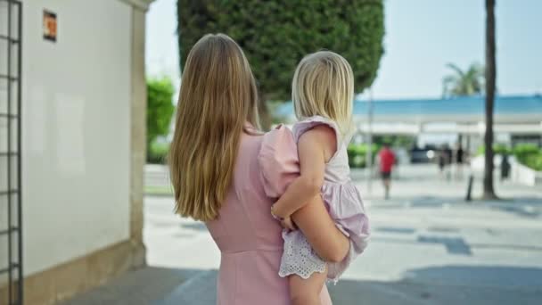 Радостная, уверенная в себе мать улыбается, держа в руках свою весёлую дочь, стоя вместе на солнечной городской улице - Кадры, видео