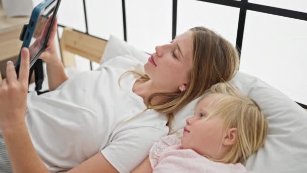 Καυκάσια μητέρα και κόρη ξαπλωμένες στο κρεβάτι βλέποντας βίντεο στο touchpad στο υπνοδωμάτιο - Πλάνα, βίντεο