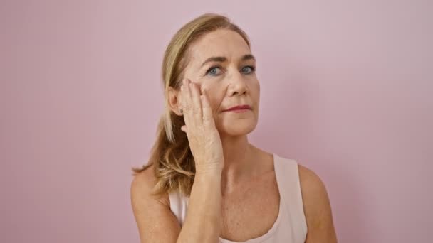 Uma mulher madura examina seu rosto contra um fundo rosa, refletindo beleza e envelhecimento. - Filmagem, Vídeo