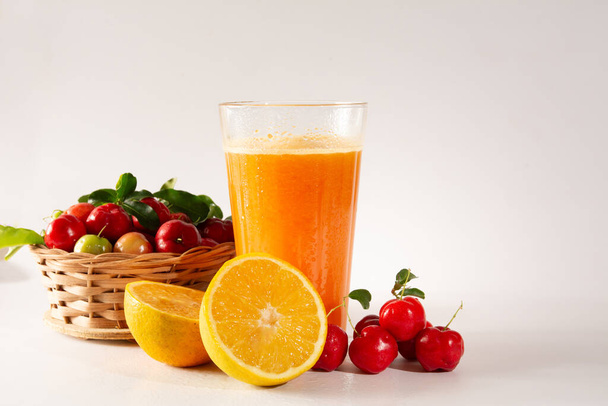 Acerola biologique frais et jus d'orange dans une tasse en verre avec demi-orange et baies d'acérola à l'intérieur d'un panier en bois dans un studio blanc propre photo en vue de l'avant - Photo, image