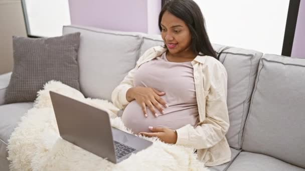 Zářivá mladá těhotná žena, užívající si mateřského odpočinku, pohodlně odpočívající doma, masírující břicho, pozitivně se usmívající na obrazovce notebooku - Záběry, video