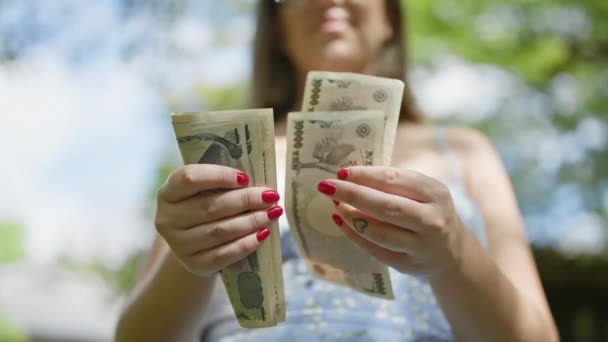 Бережная молодая женщина считает кучу иен банкнотами посреди пышной зелени традиционного японского парка, укрепляя свою финансовую свободу - Кадры, видео