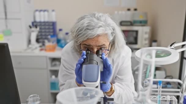 Een volwassen vrouw wetenschapper onderzoekt monsters met een microscoop in een laboratorium setting. - Video