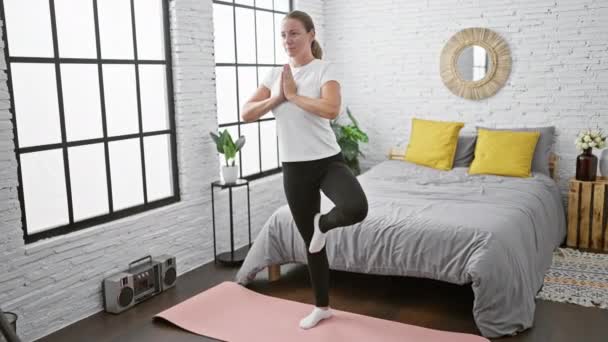 Ernsthafte junge blonde Frau findet ruhigen Ausgleich, konzentriert sich auf eine morgendliche Yoga-Übung, steht in ihrem Schlafzimmer - Filmmaterial, Video