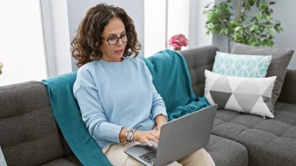 Uitgeputte vrouw van middelbare leeftijd met krullend haar sluiting laptop in een gezellige indoor setting. - Video