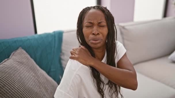 Afričanky americká žena s kudrnaté vlasy zažívá bolest krku v moderním obývacím pokoji nastavení. - Záběry, video