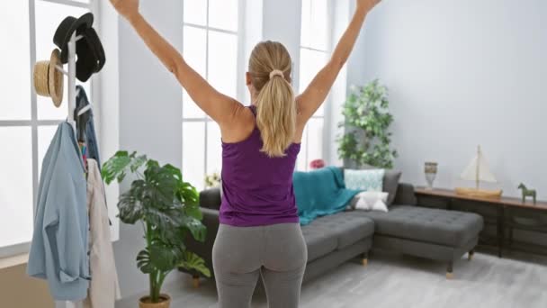 Blond vrouw stretching in woonkamer interieur van modern appartement, het bevorderen van wellness. - Video