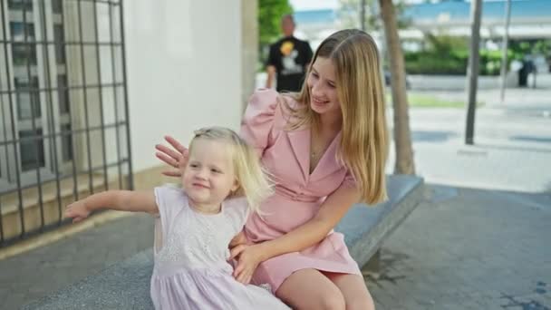 Bělošská matka a dcera, plná radosti, sedící společně na lavičce, sdílející milující polibek na rušné ulici - Záběry, video