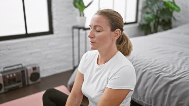Aantrekkelijke jonge blonde vrouw het vinden van evenwicht door yoga oefening, zitten op slaapkamer vloer in de ochtend sereniteit - Video