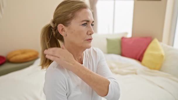 Dospělá žena zažívá bolest ramen v útulné ložnici plné barevných polštářů. - Záběry, video