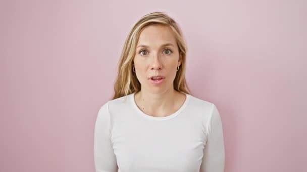 Junge blonde Frau, erstaunt und verängstigt, zeigt sich schockiert und aufgeregt über isolierten rosa Hintergrund - Filmmaterial, Video