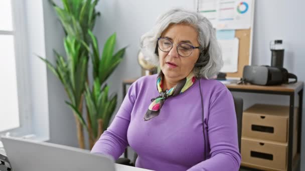 Müde reife Frau mit grauen Haaren entfernt Headset in modernen Büroräumen - Filmmaterial, Video