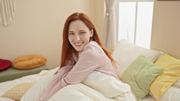 Una giovane donna caucasica sorridente sdraiata a letto, che mostra un interno confortevole ed elegante della camera da letto. - Filmati, video