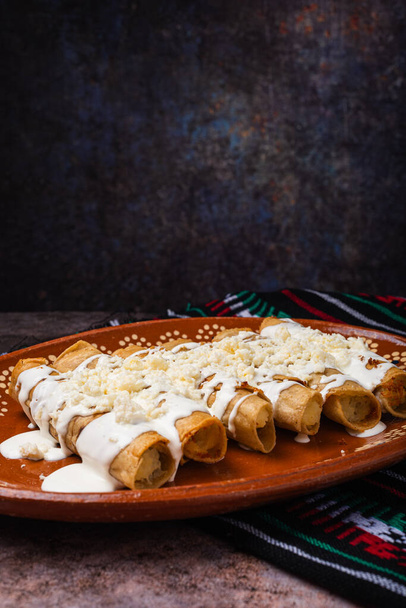 Жареный картофельный тако со сливками и сыром в мексиканской грязи. Tacos dorados, Мексиканская кухня. - Фото, изображение