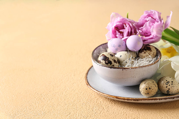 Schüssel mit Osterwachteleiern und Tulpenblüten auf beigem Tisch - Foto, Bild