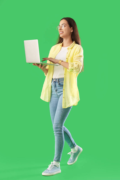 Милая молодая женщина-программист с ноутбуком идет вперед на зеленом фоне - Фото, изображение