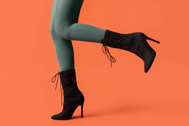 オレンジ色の背景にスタイリッシュな黒い靴で若い女性の足 - 写真・画像