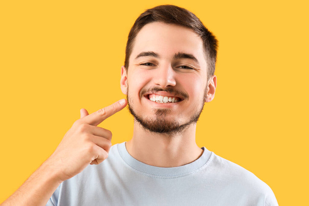 Красивый молодой человек, указывающий на здоровые зубы на желтом фоне. Концепция стоматологической помощи - Фото, изображение