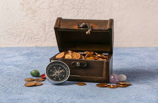 Stará truhla s mincemi, drahými kameny a kompasem na modrém grunge stolku u bílé zdi - Fotografie, Obrázek