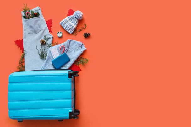 Βαλίτσα με ζεστά ρούχα, κλαδιά ελάτης, εισιτήριο και ξυπνητήρι σε πορτοκαλί φόντο. Χειμερινές διακοπές - Φωτογραφία, εικόνα