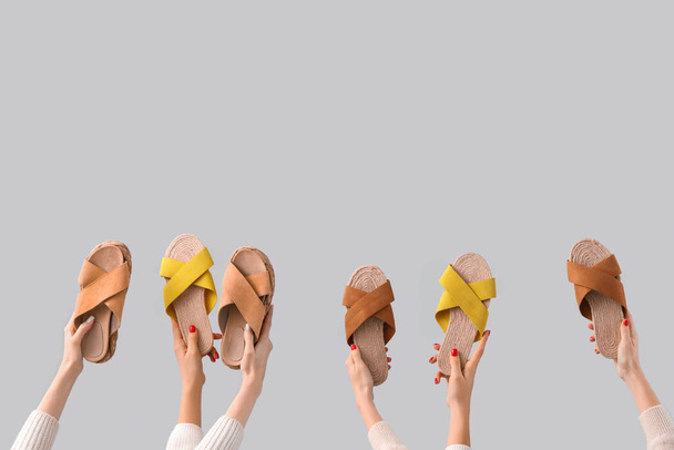 Mãos femininas segurando sandálias no fundo cinza - Foto, Imagem