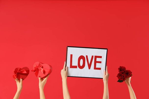 Kadın elleri çerçeveyi aşk sözcüğüyle, kalp şeklinde hediye kutularıyla ve kırmızı arka planda güllerle tutuyor. Sevgililer Günü kutlaması - Fotoğraf, Görsel