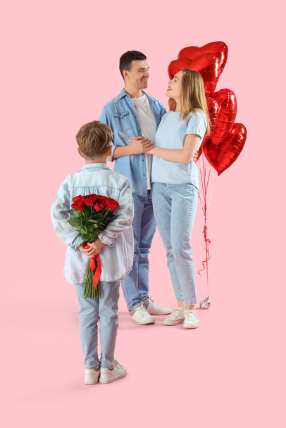 Kleine jongen met rozen en zijn ouders op roze achtergrond, achteraanzicht. Valentijnsdag - Foto, afbeelding