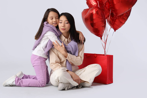 Young Asian woman and her little daughter with heart-shaped air balloons on white background. Valentine's day celebration - Photo, Image