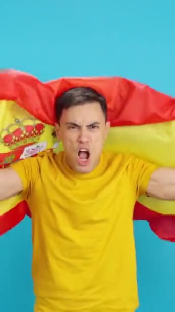 Video in studio with blue background of a man dancing and encouraging with a Spanish flag unfurled. The frame starts empty, the man appears from below and then disappears at the bottom. - Footage, Video