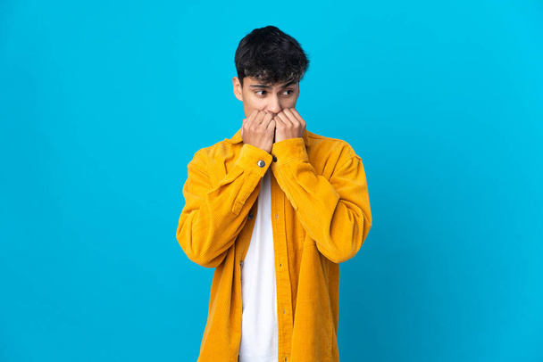 Молодой человек на изолированном синем фоне нервничает и боится положить руки в рот
 - Фото, изображение