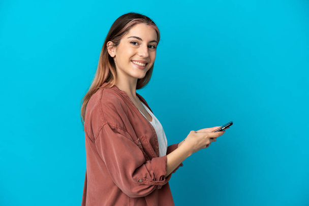 青い背景に隔離された若い白人女性携帯電話でメッセージや電子メールを送る - 写真・画像