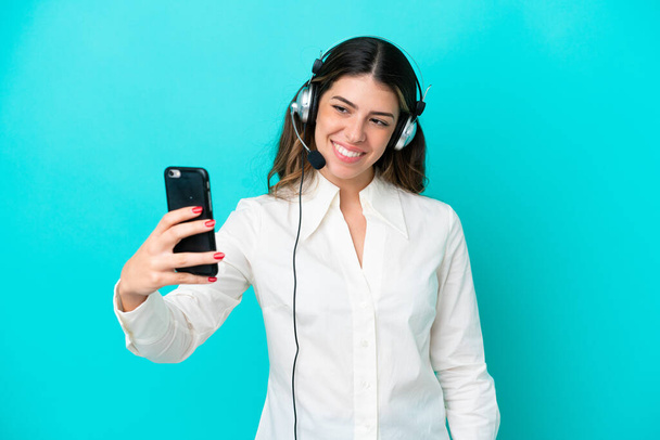 Telemarketer Italian woman working with a headset isolated on blue background making a selfie - Photo, Image