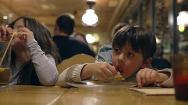 Niño pequeño comiendo rebanada de pizza en el restaurante, Niño disfrutando de la nutrición de carbohidratos en el restaurante por la noche - Imágenes, Vídeo