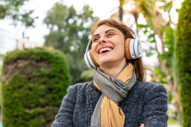 Açık havada müzik dinleyen esmer kadın mutlu ve gülümsüyor. - Fotoğraf, Görsel