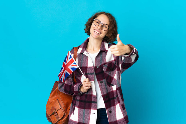 Junge Engländerin mit einer britischen Flagge auf blauem Hintergrund und erhobenem Daumen, weil etwas Gutes passiert ist - Foto, Bild