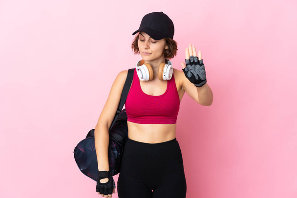 Jonge sportvrouw met sporttas over geïsoleerde achtergrond maken stop gebaar en teleurgesteld - Foto, afbeelding