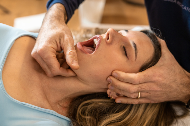 An osteopath performs a jaw adjustment on a female patient, focusing on alleviating tension and improving joint function. - Photo, Image