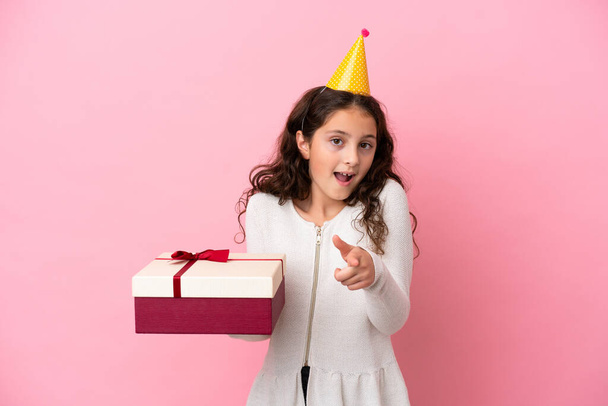 Kleine kaukasische Mädchen mit einem Geschenk isoliert auf rosa Hintergrund überrascht und zeigt nach vorne - Foto, Bild