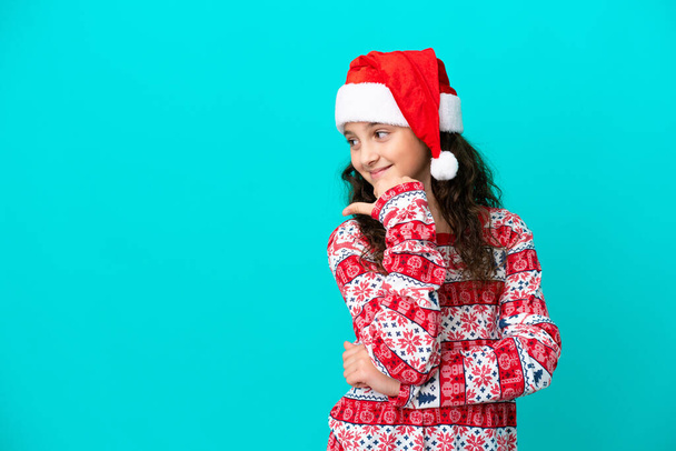 Piccolo caucasico con cappello di Natale isolato su sfondo blu che punta verso il lato per presentare un prodotto - Foto, immagini
