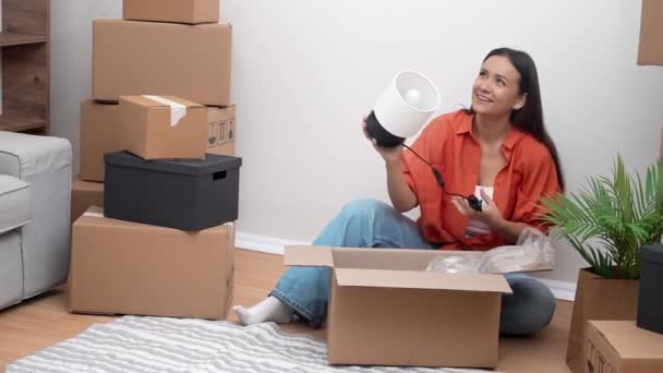 Ελκυστικό θηλυκό ανοίγει μεγάλα κουτιά συσκευασίας στο πάτωμα σε νέο σπίτι εξετάζει την ακεραιότητα των διαφόρων μεταφερόμενων επίπλων σε νέο σπίτι στην ύπαιθρο - Πλάνα, βίντεο