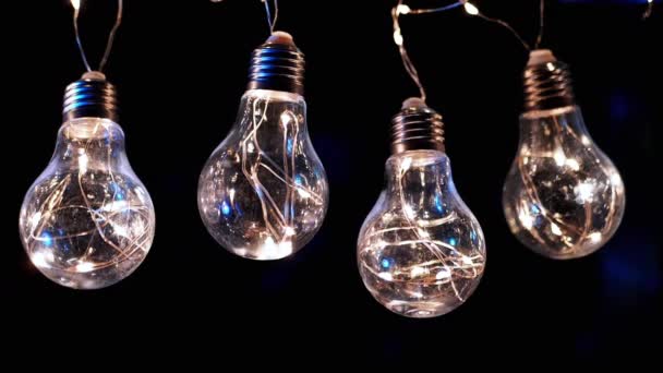 Lampadine Vintage Edison incandescenti appese a soffitto su sfondo nero. Di fila. Luce calda. Filo. Decorazioni natalizie, lampadine elettriche vintage in stile retrò ghirlanda illuminano lo spazio. - Filmati, video