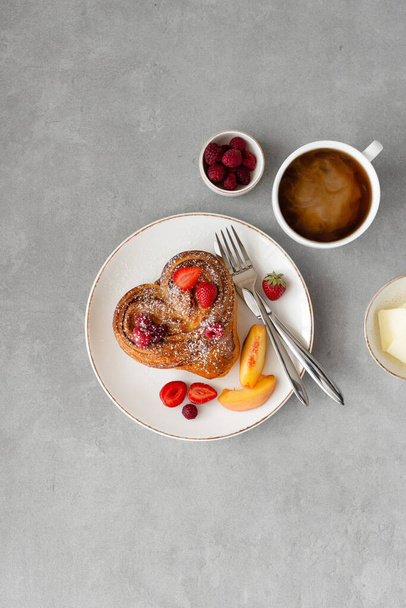 Desayuno de San Valentín sobre fondo gris. Pan con mantequilla y bayas en un plato blanco y una taza de café. Vista superior, espacio de copia - Foto, imagen